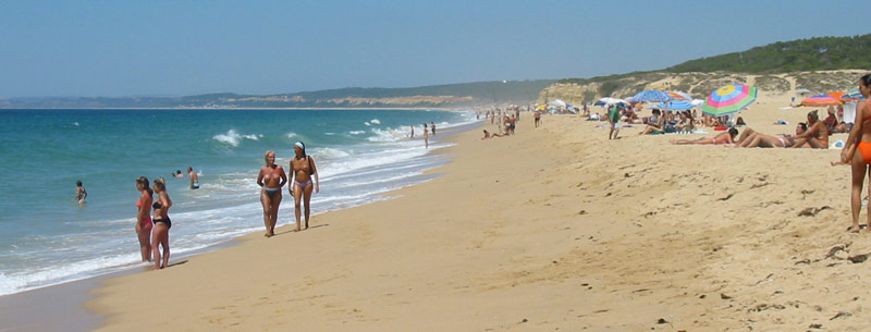 The wide, beautiful sandy beach and rolling blue waves of the Atlantic Ocean at Praia do Meco on a hot summer day