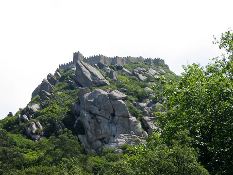 The ancient stone battlements and towers of the Moorish Castle crowning the rocky, forested peaks above Sintra